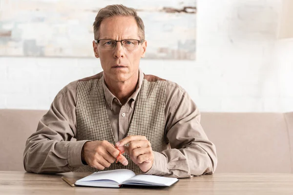 Upset senior man with alzheimers disease string human finger reminder sitting near notebook — Stock Photo