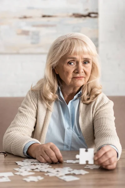 Enfoque selectivo de la mujer jubilada confundida con alzheimer celebración de la pieza del rompecabezas - foto de stock