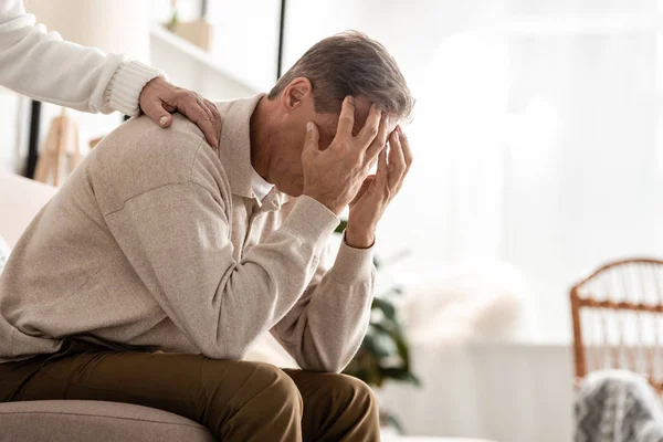 Cropped view of retired woman touching sick husband covering face — Stock Photo