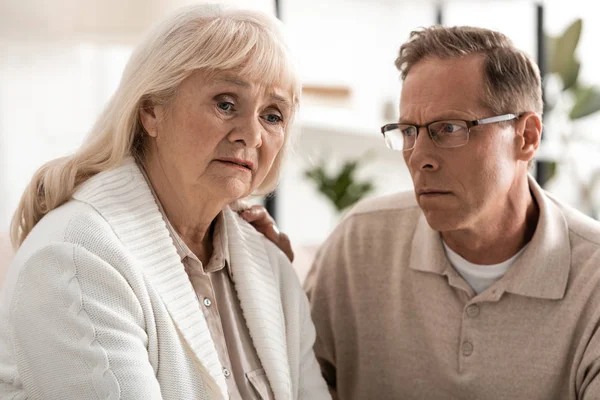 Bouleversé homme âgé dans des lunettes regardant femme malade avec alzheimer — Photo de stock