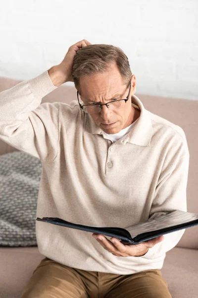 Nachdenklicher Mann mit Alzheimer-Brille hält Fotoalbum zu Hause — Stockfoto