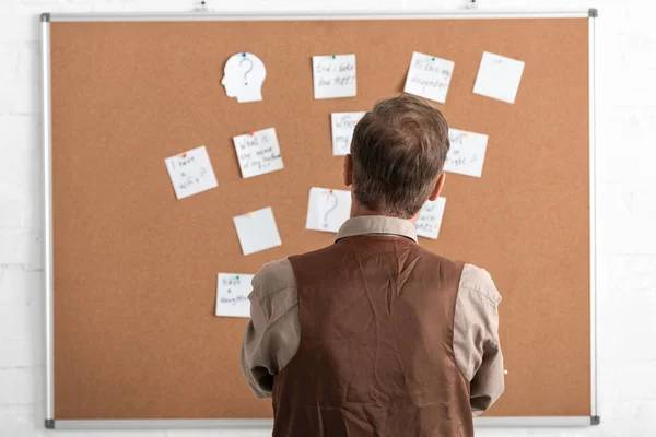 Back view of sick senior man standing near board with papers — Stock Photo