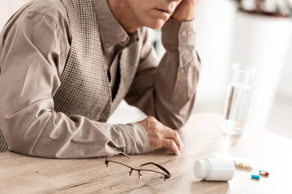 Cropped view of sad senior man sitting near pills on table — Stock Photo