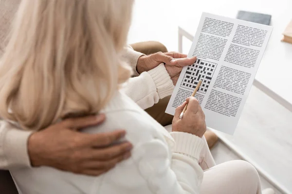 Vue recadrée de senior homme étreignant femme avec crayon et mots croisés — Photo de stock