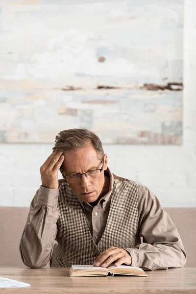 Sick senior man with dyslexia sitting and reading book at home — Stock Photo