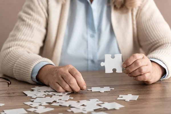 Обрезанный вид женщины на пенсии с Альцгеймером, держащей кусочек головоломки — стоковое фото