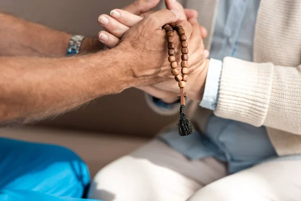 Cropped view of doctor with rosary beads holding hands of senior woman — Stock Photo