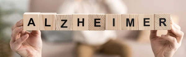 Panoramic shot of senior woman holding wooden cubes with alzheimer letters — Stock Photo