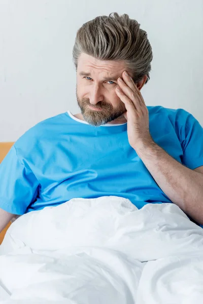 Beau patient en robe médicale ayant mal à la tête à l'hôpital — Photo de stock