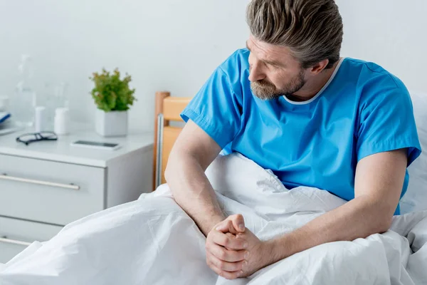 Patient in medical gown with clenched hands looking away in hospital — Stock Photo