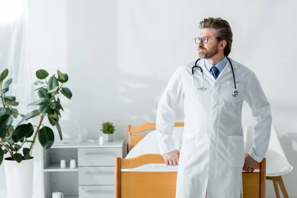 Guapo médico de bata blanca mirando hacia otro lado en el hospital - foto de stock