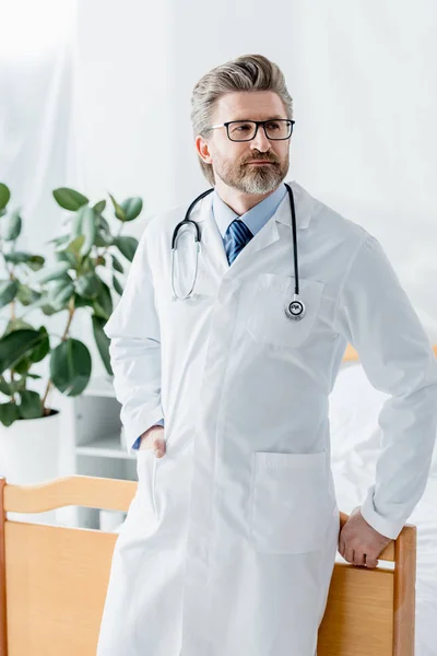 Médico bonito em casaco branco olhando para longe no hospital — Fotografia de Stock