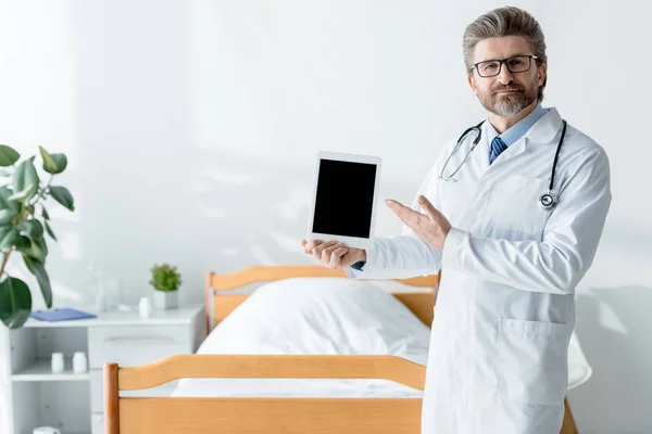 Bel dottore in camice bianco che punta con mano al tablet digitale in ospedale — Foto stock