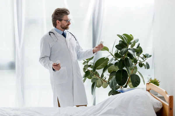 Красивый доктор в белом халате держит бутылки с таблетками в больнице — стоковое фото