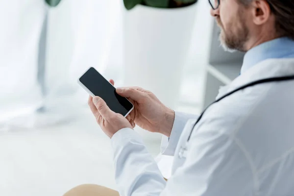 Vista recortada del médico en bata blanca usando teléfono inteligente en el hospital - foto de stock
