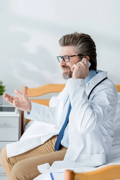 Smiling doctor in white coat talking on smartphone in hospital — Stock Photo