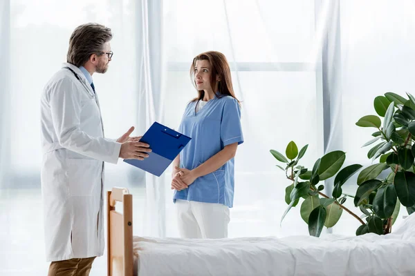 Doctor en bata blanca hablando con atractiva enfermera en el hospital - foto de stock