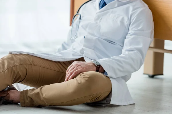 Ausgeschnittene Ansicht eines Arztes im weißen Mantel, der im Krankenhaus auf dem Boden sitzt — Stockfoto