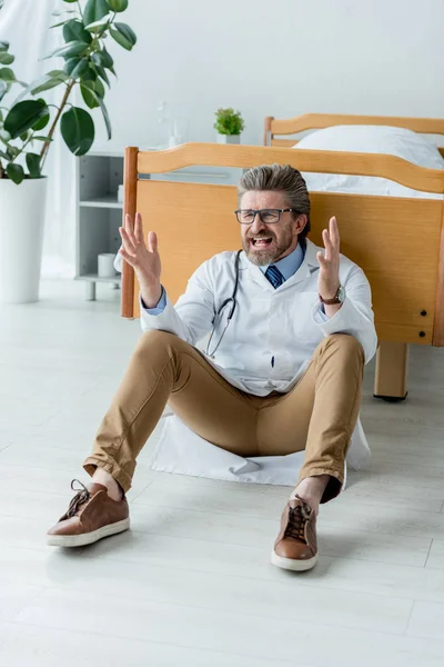 Angry doctor in white coat sitting on floor and screaming in hospital — Stock Photo