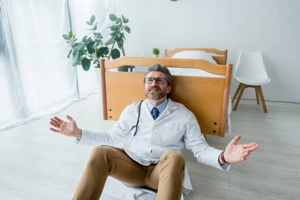 Triste médecin en manteau blanc assis sur le sol avec les mains tendues à l'hôpital — Photo de stock