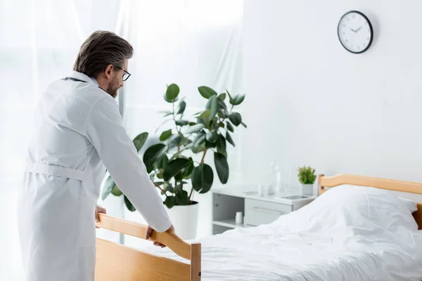 Back view of doctor in white coat looking at bed in hospital — Stock Photo