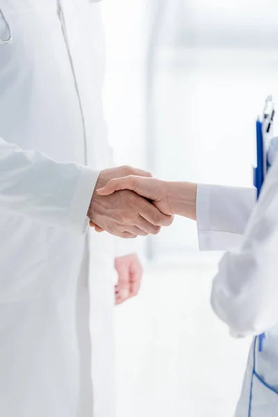 Cropped view of doctors in white coats shaking hands in hospital — Stock Photo