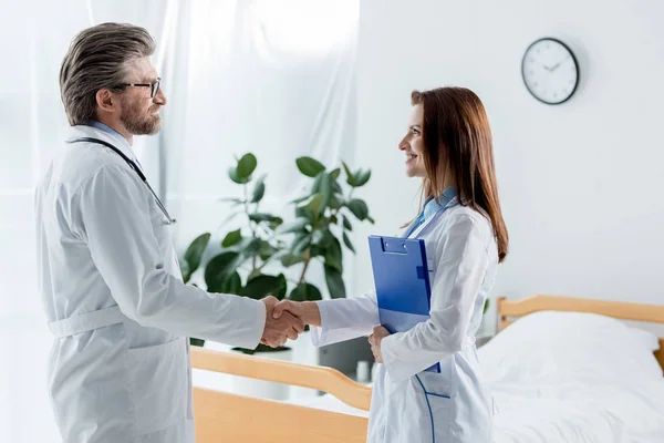 Arzt im weißen Mantel und sein lächelnder Kollege beim Händeschütteln im Krankenhaus — Stockfoto