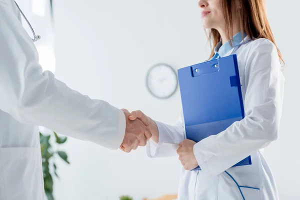 Vista recortada del médico de bata blanca y su colega estrechando la mano en el hospital - foto de stock