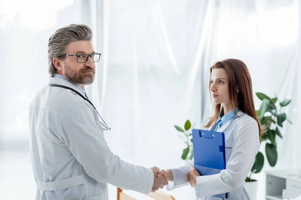 Médico de bata blanca y su colega estrechando las manos en el hospital - foto de stock