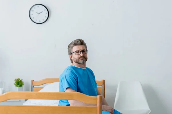 Пациент в медицинском халате сидит на кровати в больнице — стоковое фото