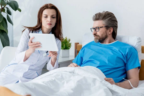Doctor en bata blanca y paciente mirando tableta digital en el hospital - foto de stock