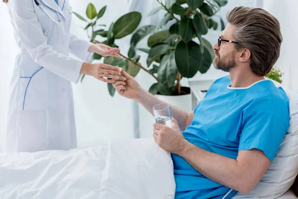 Обрізаний вид лікаря в білому пальто дає таблетку пацієнту в лікарні — стокове фото