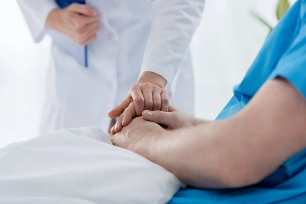 Ausgeschnittene Ansicht eines Arztes im weißen Mantel, der die Hand eines Patienten im Krankenhaus hält — Stockfoto
