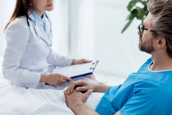 Обрезанный вид врача в белом халате, смотрящего на пациента в больнице — стоковое фото