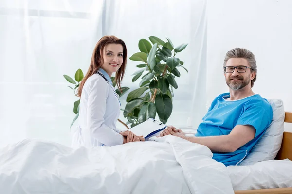 Улыбающийся доктор в белом халате и пациент смотрит на камеру в больнице — стоковое фото