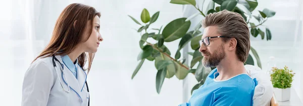 Panoramic shot of doctor in white coat looking at patient in hospital — Stock Photo