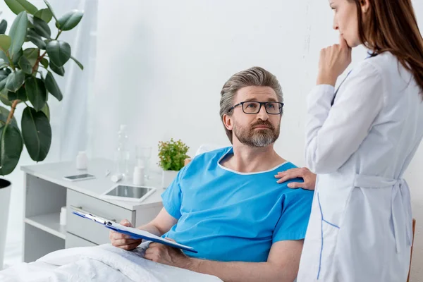Médico de bata blanca hablando con el paciente con portapapeles en el hospital - foto de stock