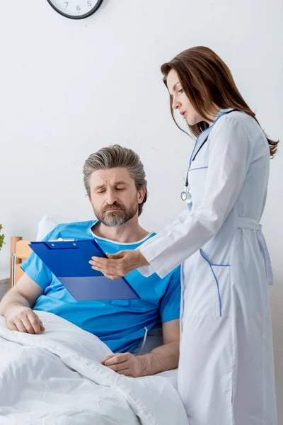 Doctor in white coat showing clipboard to patient in hospital — Stock Photo