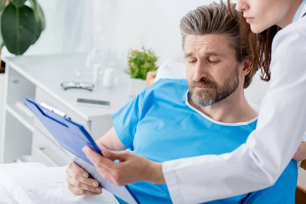 Cropped view of doctor showing clipboard to patient in hospital — Stock Photo