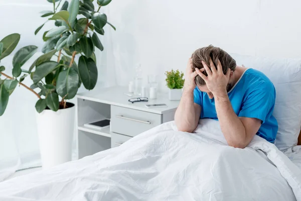 Sad patient in medical gown touching head in hospital — Stock Photo
