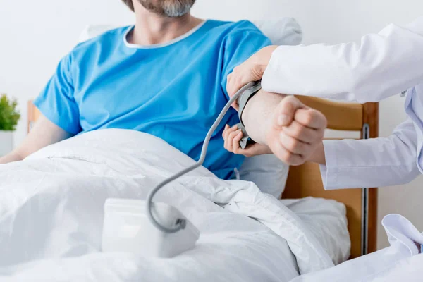 Vista recortada del médico midiendo la presión arterial del paciente en el hospital - foto de stock