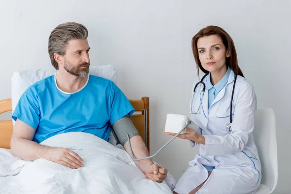 Doctor in white coat measuring blood pressure of patient in hospital — Stock Photo