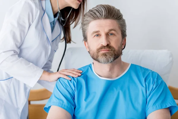 Обрезанный взгляд врача в белом халате на пациента со стетоскопом в больнице — стоковое фото