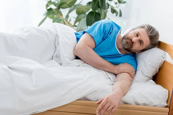 Guapo paciente en bata médica acostado en la cama en el hospital - foto de stock