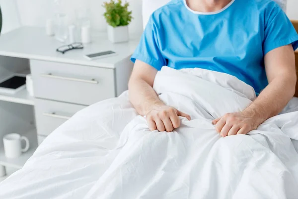 Vista cortada do paciente em vestido médico sentado na cama no hospital — Fotografia de Stock