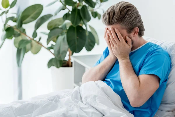 Paciente triste em vestido médico sentado na cama e chorando no hospital — Fotografia de Stock