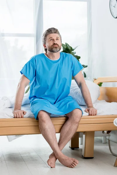 Patient en robe médicale assis sur le lit et regardant vers le haut à l'hôpital — Photo de stock