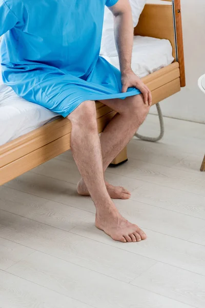 Vista cortada do paciente em vestido médico sentado na cama no hospital — Fotografia de Stock