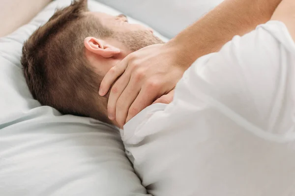 Young man lying in bed and suffering from neck pain — Stock Photo