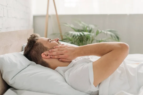Junger Mann berührt Wange im Bett und leidet unter Zahnschmerzen — Stockfoto